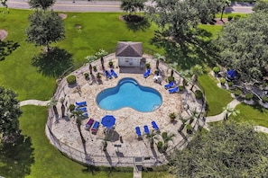 An aerial view of a circular pool area with lounge chairs and a small building, surrounded by a fence and greenery. - Magnolia Place 4665-104 (Myrtle Beach)