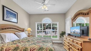 A bedroom with a bed, a television, a dresser, a ceiling fan, and a window with a view of the outdoors. - Magnolia Place 4665-104 (Myrtle Beach)