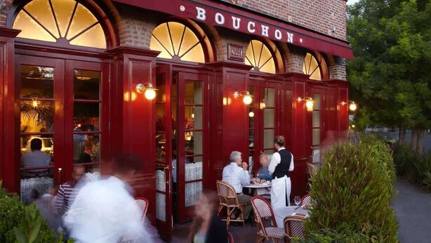 Un restaurant doté d’une terrasse, d’une façade en briques et d’une enseigne portant l’inscription « BOUCHON ».