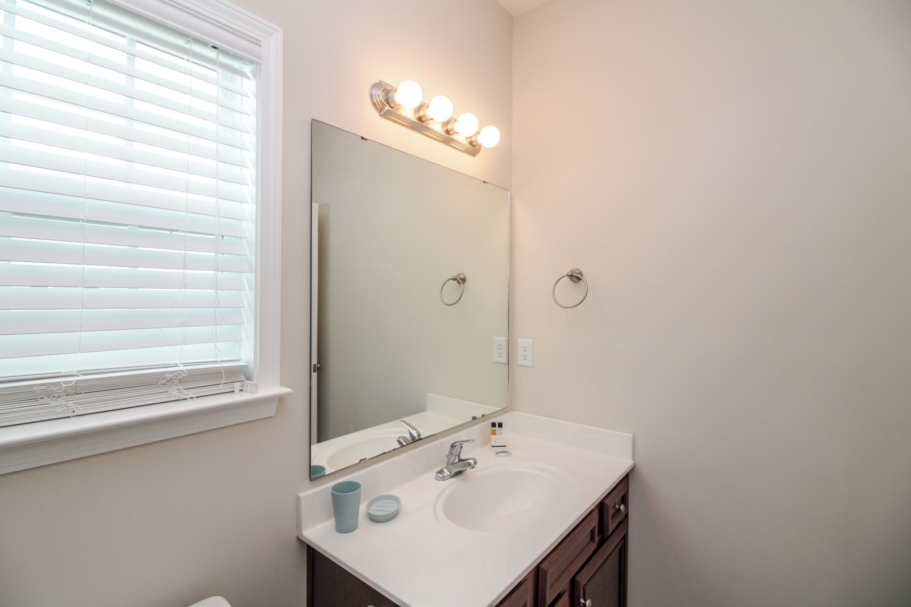A bathroom with a large mirror, vanity, and a window with blinds.