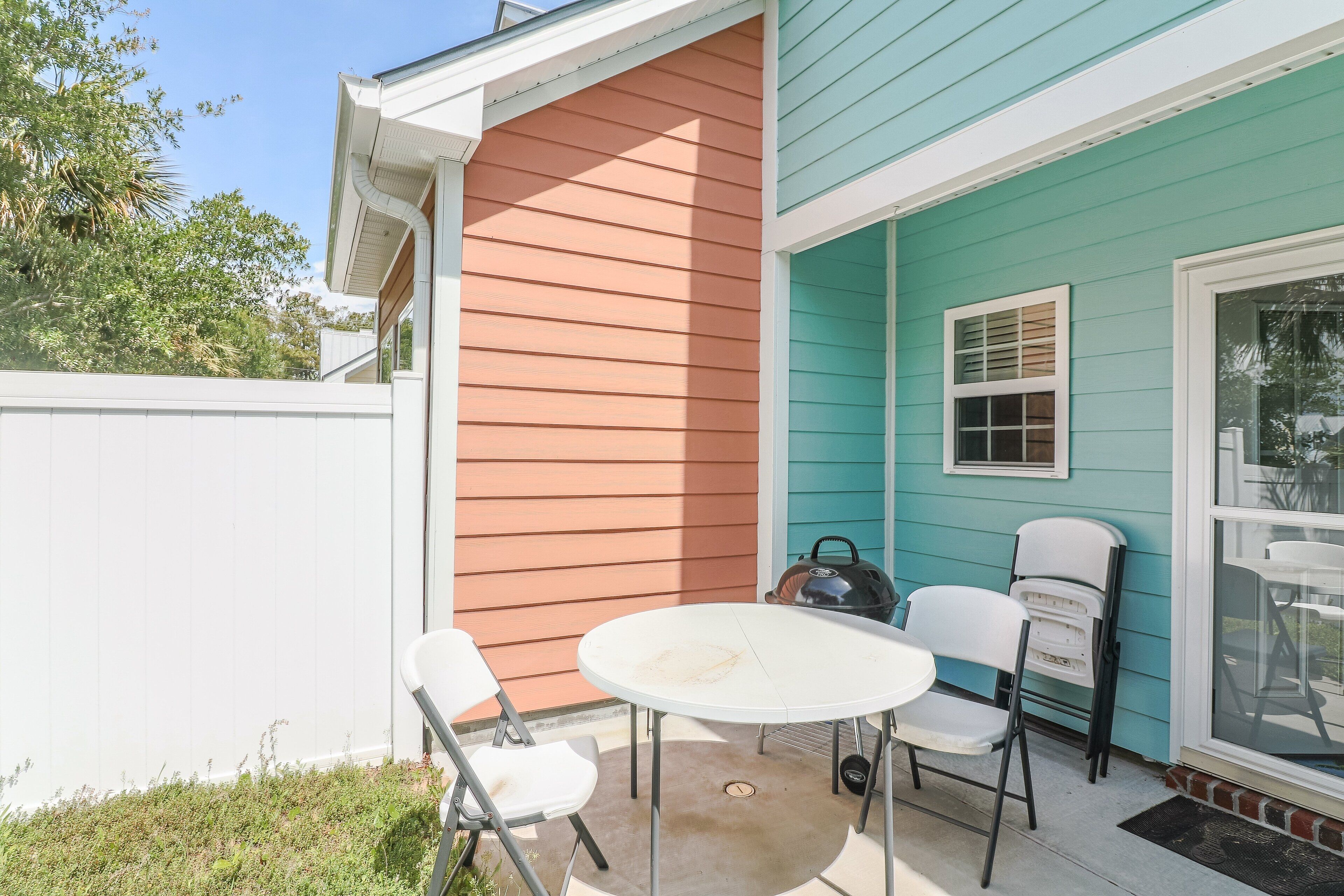 An outdoor patio with a round table and white chairs, adjacent to a house with two-tone siding.