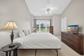 Ein Schlafzimmer mit einem Bett, einer Lampe, einem Fernseher und Blick ins Freie durch eine Tür.