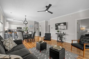 Ein modernes Wohnzimmer mit grauem Sofa, schwarzem Hocker und Deckenventilator.