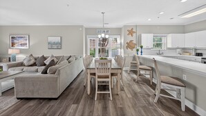A modern kitchen with white cabinets, a central island, and a dining area with a light-colored table and chairs. - Magnolia North 4819-105 (Myrtle Beach)