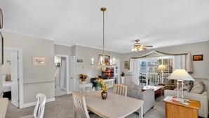 A spacious living room with a dining area, a ceiling fan, and a large window providing natural light. - Magnolia Place 4631-204 (Myrtle Beach)