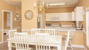 A dining area with a white table and chairs, a chandelier, and a kitchen with white cabinets and appliances. - Magnolia Place 4665-301 (Myrtle Beach)