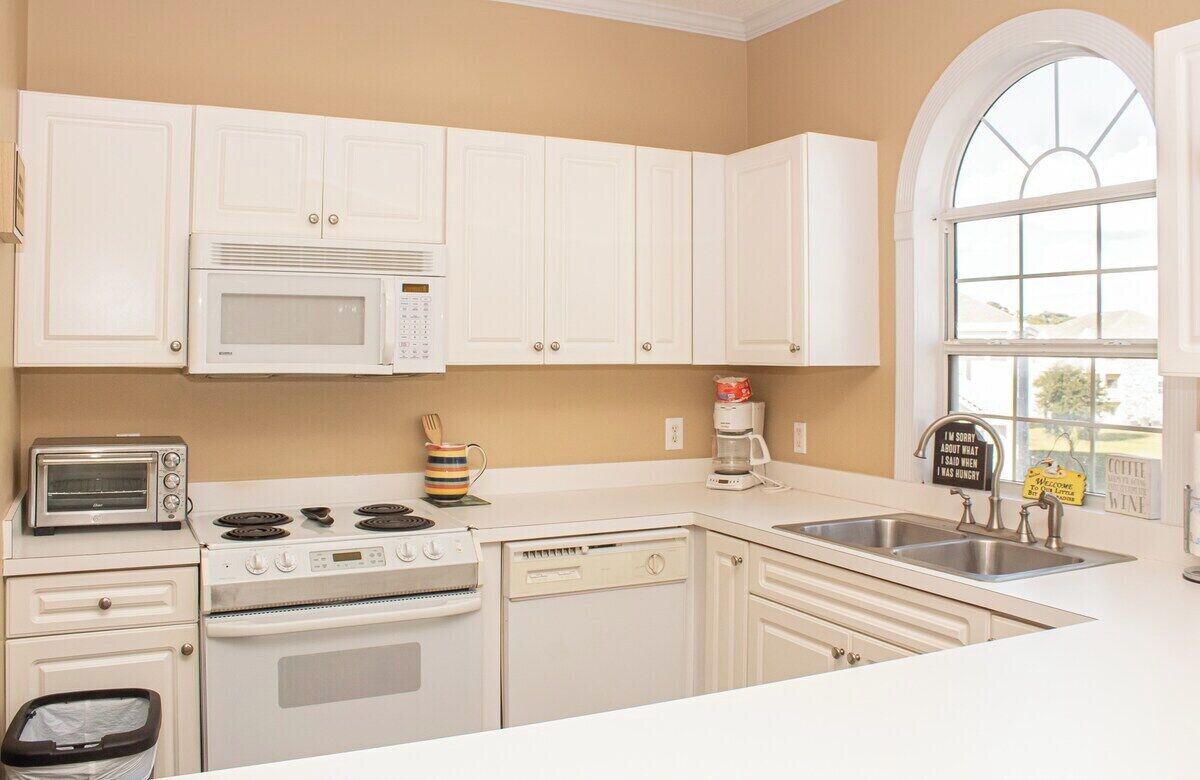 A kitchen with white cabinets, a microwave, a stove, a dishwasher, a toaster, and a sink.