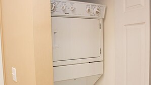 A laundry room with a white washer and dryer, a door, and a light switch on the wall. - Magnolia Place 4665-301 (Myrtle Beach)
