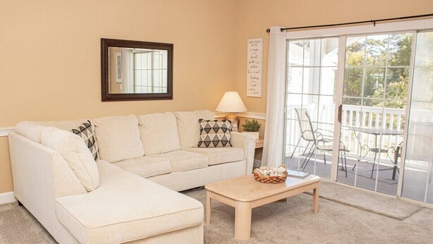 A living room with a beige sofa, a wooden coffee table, and a glass door leading to an outdoor patio. - Magnolia Place 4665-301 (Myrtle Beach)