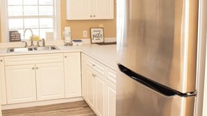 A kitchen with white cabinets, a stainless steel refrigerator, a window with a view, and a 'Friends gather here' sign. - Magnolia Place 4665-301 (Myrtle Beach)