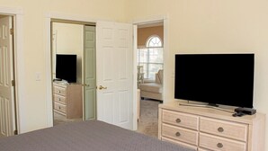 A bedroom with a large bed, a dresser with drawers, a television, and a door leading to another room. - Magnolia Place 4665-301 (Myrtle Beach)