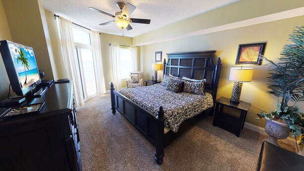 A bedroom with a bed, a ceiling fan, a TV, and a potted plant. - Ocean Blue 602 (Myrtle Beach)