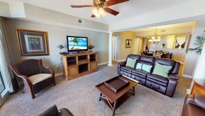 A living room with a brown leather sofa, a wicker chair, a wooden entertainment unit with a TV, and a ceiling fan. - Ocean Blue 602 (Myrtle Beach)