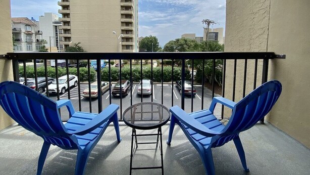 A balcony with two blue chairs and a small table, overlooking a parking lot and buildings. - Ocean Dunes 6011 (Myrtle Beach)