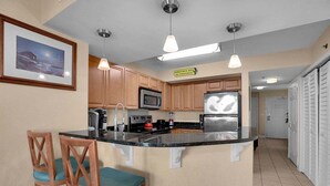 A kitchen with wooden cabinets, a central island with seating, a microwave, a stove, and a refrigerator. - Horizon 701 (Myrtle Beach)
