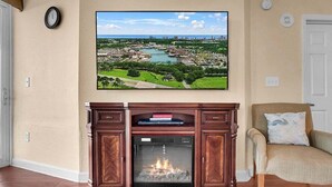A living room with a fireplace, a large wall-mounted TV displaying a scenic view, and a comfortable armchair. - Horizon 701 (Myrtle Beach)