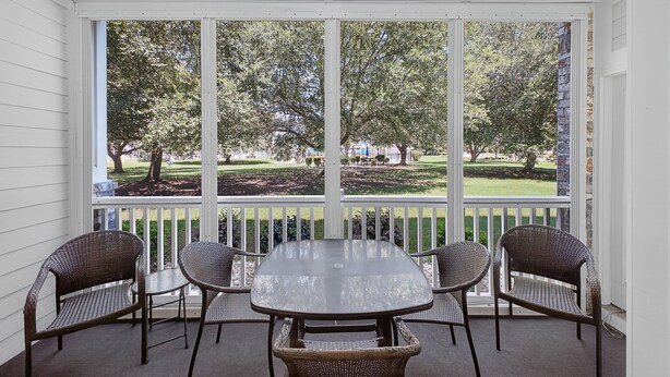A covered patio with a table and four wicker chairs, overlooking a well-maintained lawn and trees. - Magnolia Place 4639-103 (Myrtle Beach)