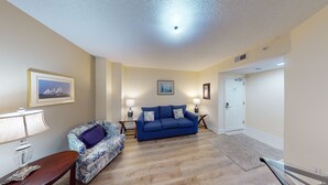 A living room with a blue sofa, a patterned armchair, a small table with a lamp, and two wall-mounted lamps. - Ocean Blue 401 (Myrtle Beach)