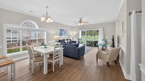 A spacious living room with a large window, a dining area, and a blue sofa. - Magnolia Place 4661-101 (Myrtle Beach)
