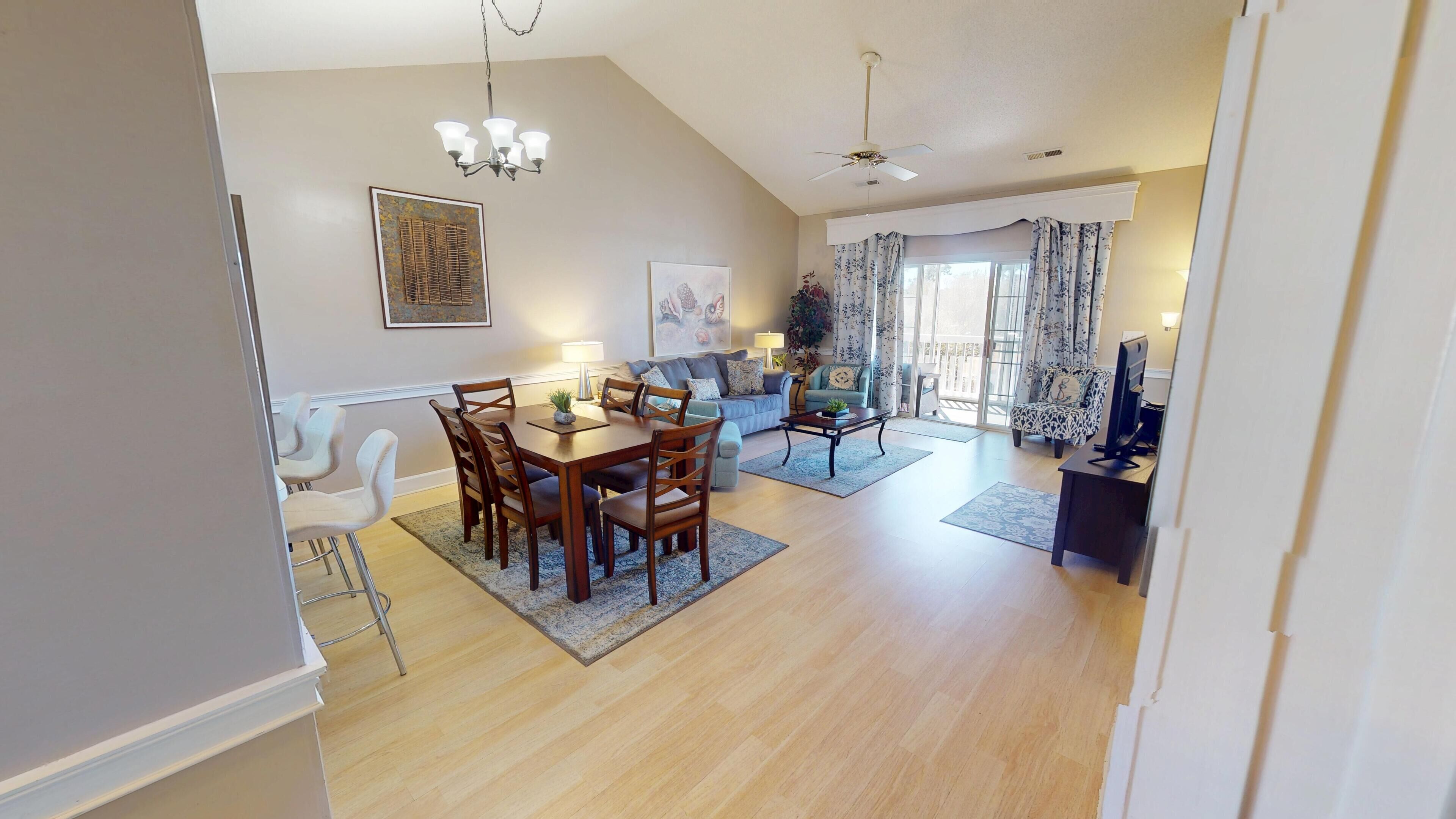 A spacious living area with a dining table and chairs, a sofa, and a television.