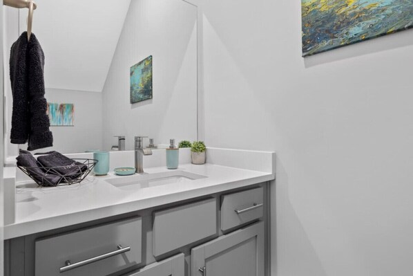 A modern bathroom with a large mirror, grey cabinets, a white countertop, and a small potted plant. - Rhythm and View - Broadway, Groups, Secure Garage (Nashville)