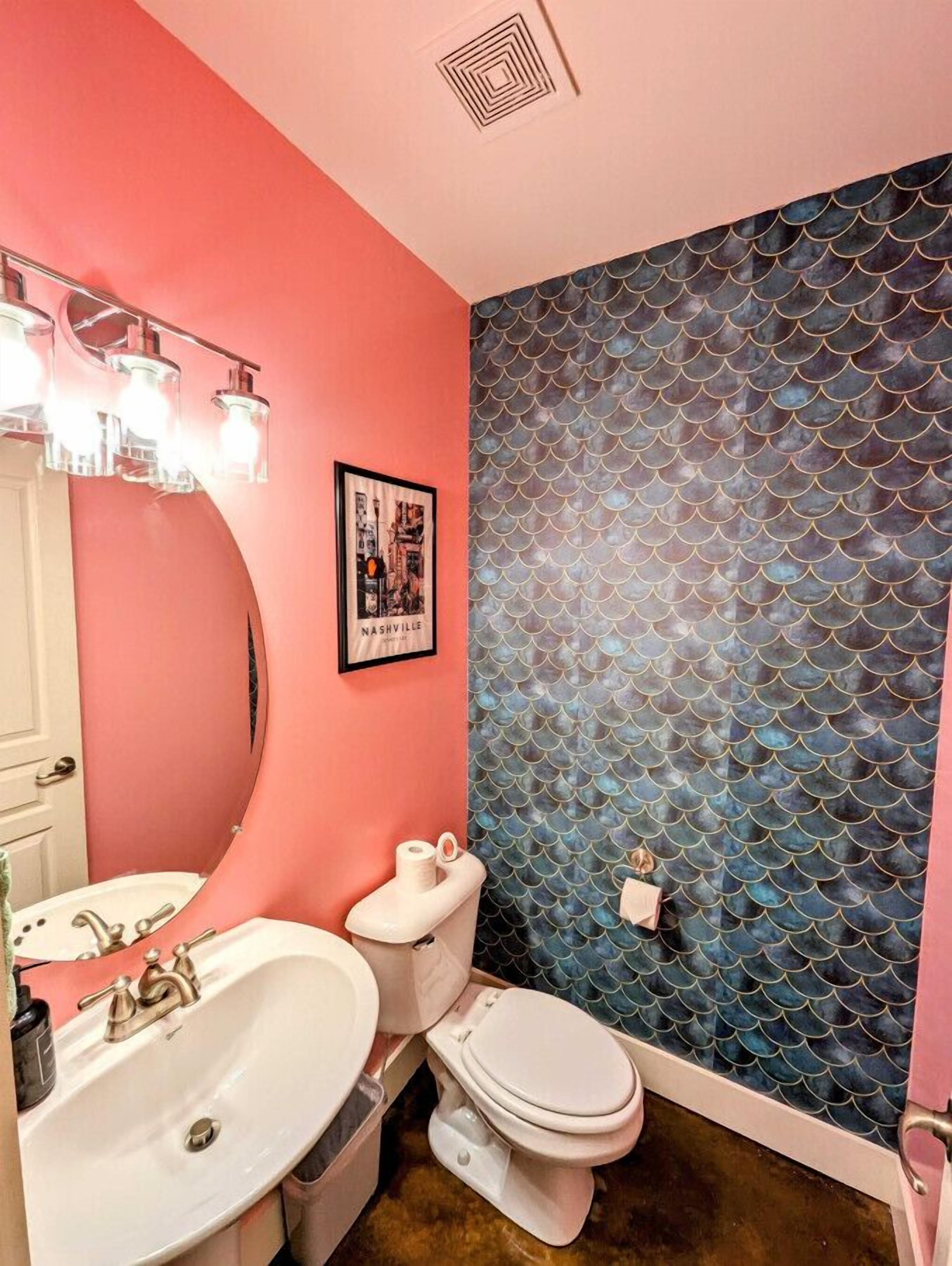 Ein Badezimmer mit einer rosa Wand, einer blauen Fliesenwand, einem weißen Waschbecken, einer Toilette und einem gerahmten Bild an der Wand.
