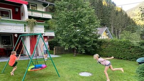 Un jardin à l’arrière d’une maison, avec une balançoire, un trampoline et une pelouse verdoyante.