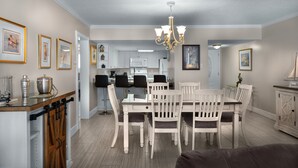 A dining area with a white table and chairs, a chandelier, and framed pictures on the walls. - Brigadune 12F (Myrtle Beach)