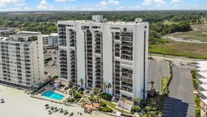 A high-rise hotel with multiple balconies, a swimming pool, and a parking area. - Brigadune 12F (Myrtle Beach)