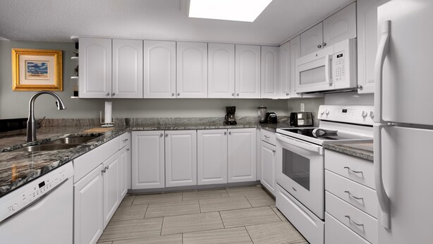 A modern kitchen with white cabinets, a granite countertop, a built-in microwave, and a stainless steel refrigerator. - Brigadune 12F (Myrtle Beach)