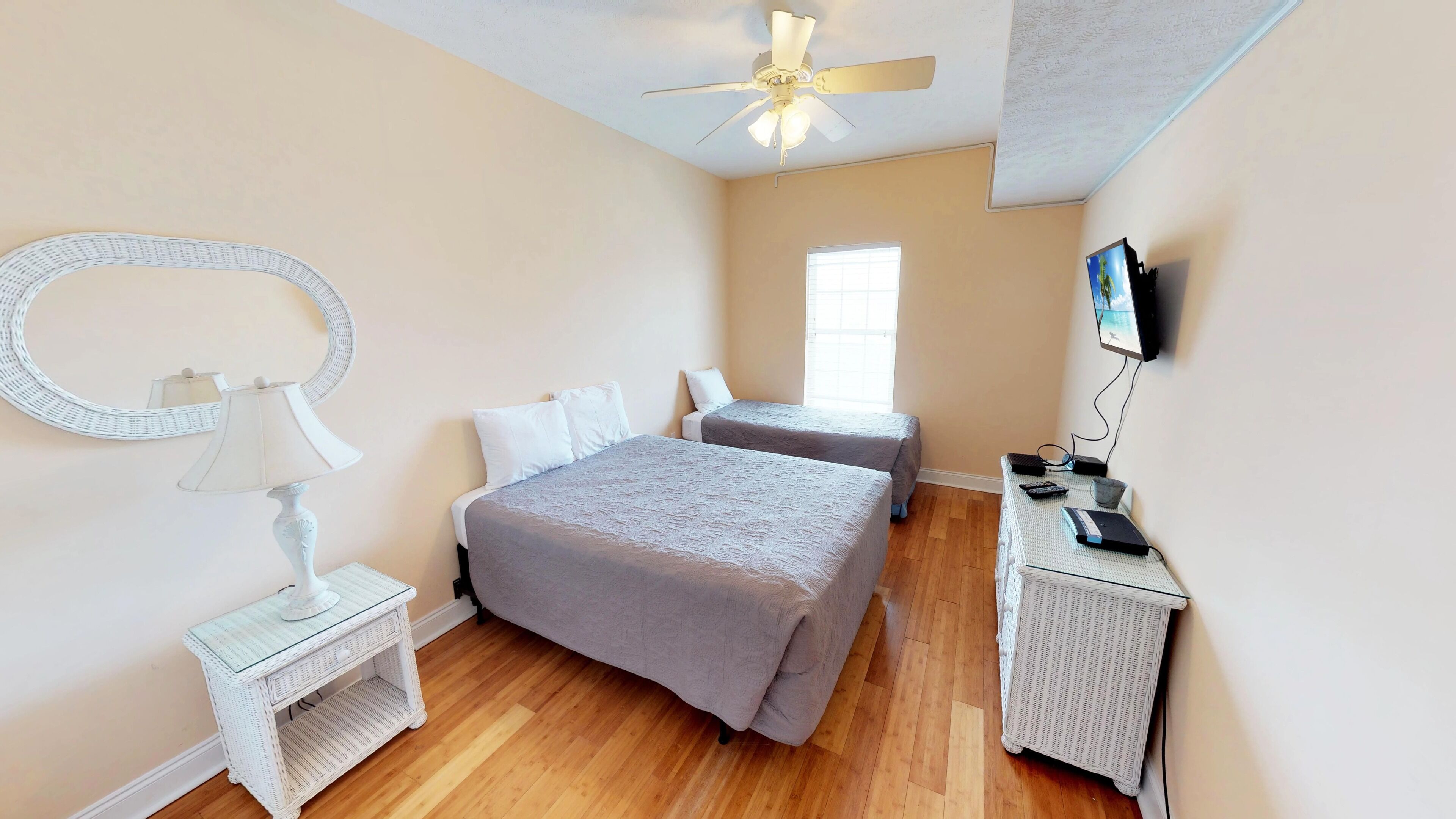 A bedroom with two beds, a ceiling fan, a TV, and a small table with a lamp.