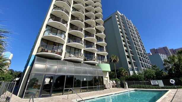 Un hôtel de grande hauteur doté de nombreux balcons, d’une piscine et surplombant un ciel d’un bleu limpide.