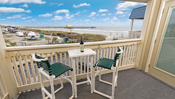 A balcony with two chairs and a table, overlooking a beach and a pier. - A Place at the Beach IV G328 (Myrtle Beach)