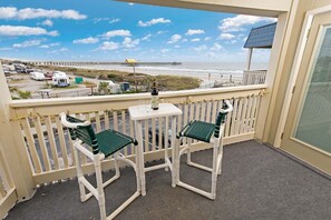 Ein Balkon mit zwei Stühlen und einem Tisch, mit Blick auf einen Strand und einen Steg.