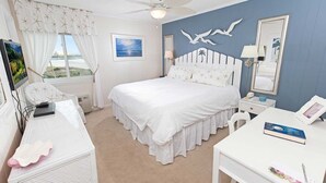 A bedroom with a bed, a desk, a chair, a ceiling fan, a window with curtains, a painting, and a wall with a seagull decoration. - A Place at the Beach IV G328 (Myrtle Beach)