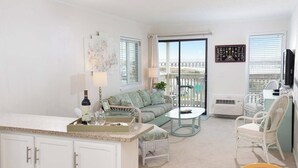 A well-lit living room with a sofa, a coffee table, and a dining area. There is a balcony with a view of the city. - A Place at the Beach IV G328 (Myrtle Beach)