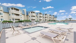 A pool area with lounge chairs and a swimming pool, surrounded by multi-story buildings with balconies. - A Place at the Beach IV G328 (Myrtle Beach)