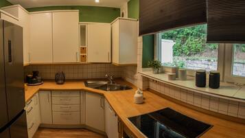 Eine moderne Küche mit weißen Schränken, einem Edelstahlkühlschrank, einem eingebauten Backofen und einem Fenster mit Blick auf Grünflächen.