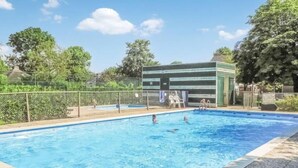 Uma piscina retangular com água azul cristalina, rodeada por uma cerca e árvores.