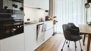 A modern kitchen with white cabinets, a black stove, and a wooden dining table with chairs. - Stillvolle Luxus Wohnung in der Residenz Silvretta by Interhome (See)