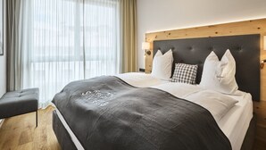 A modern hotel room with a large bed, a wooden headboard, and a view of the city through sheer curtains. - Stillvolle Luxus Wohnung in der Residenz Silvretta by Interhome (See)