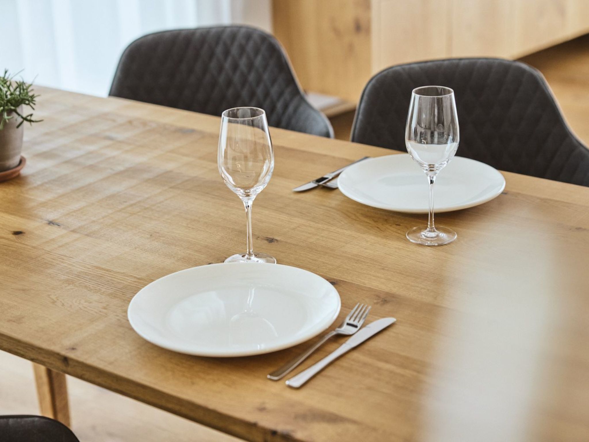 A wooden dining table with two white plates, a wine glass, and cutlery.