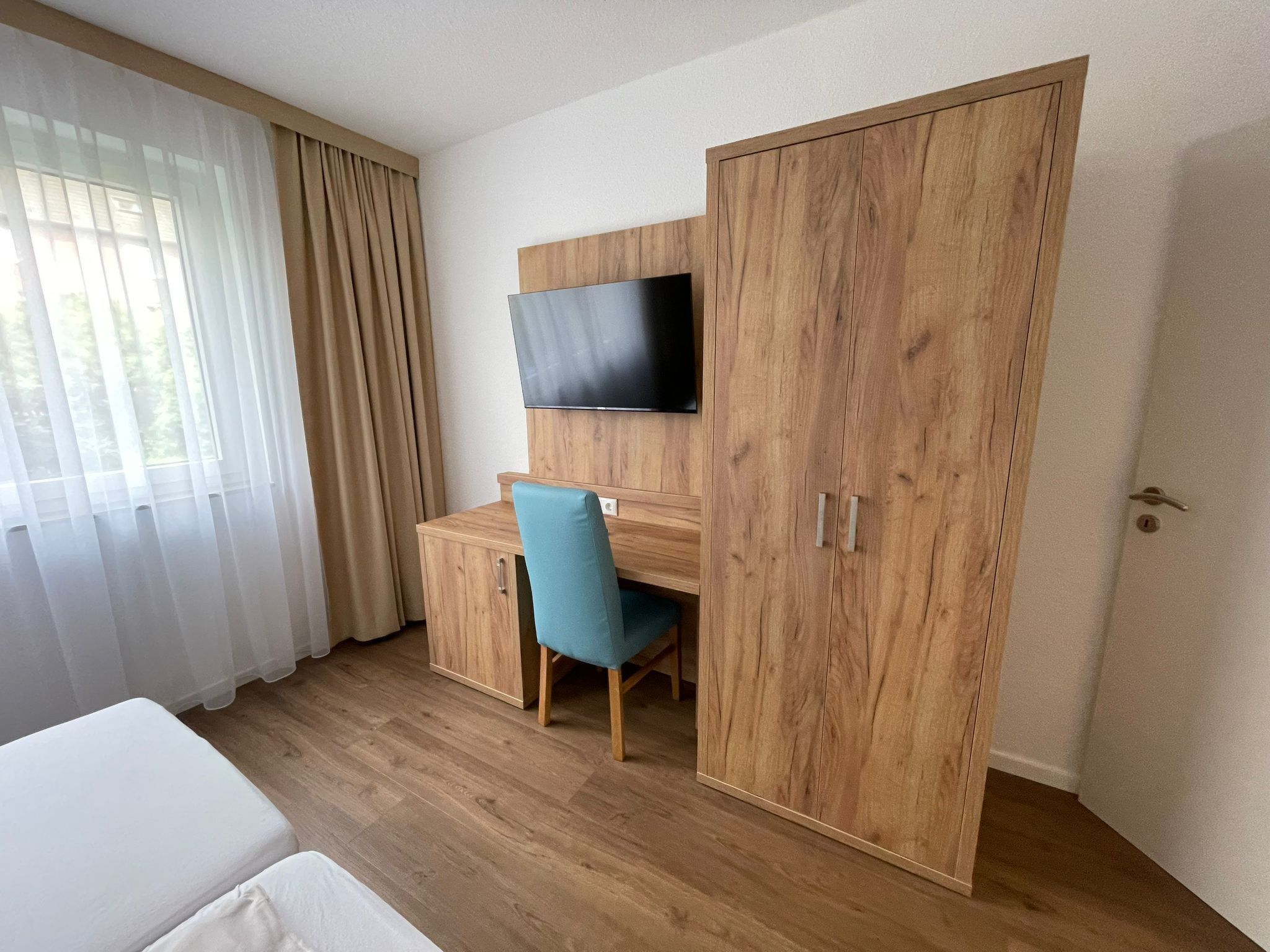 Un dormitorio con una cama, un escritorio con silla, un armario y un televisor montado en la pared.