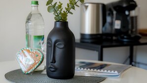 Een tafel met een zwarte vaas met groene planten, een waterfles, een hartvormig koekje en een notitieboekje.