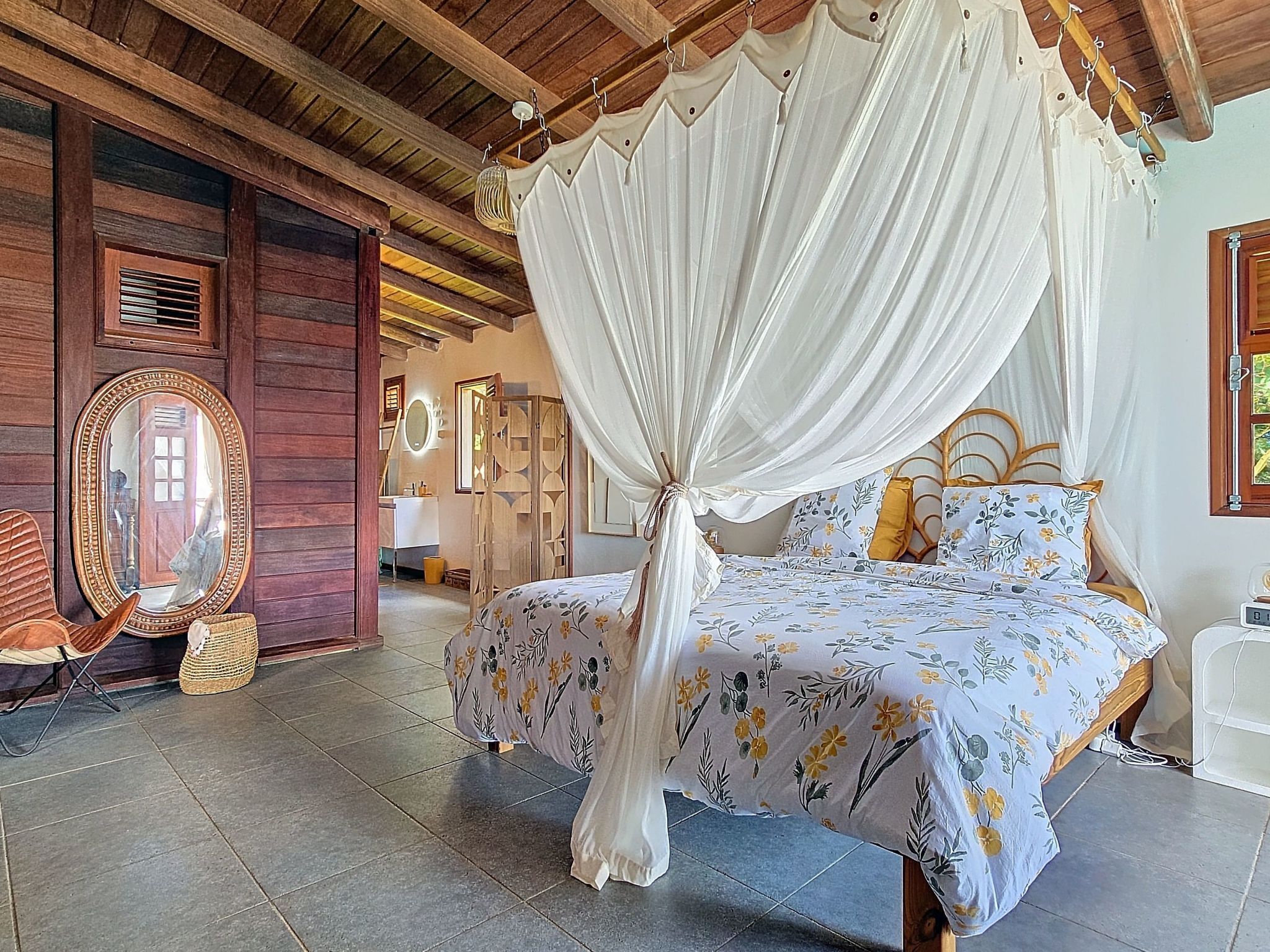 A room with a bed under a canopy, a mirror, and a wooden ceiling.