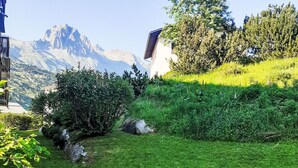 Un espace extérieur verdoyant, avec un bâtiment, des arbres et des montagnes en arrière-plan.
