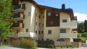 Un immeuble résidentiel à plusieurs étages, doté de balcons, d’un espace de stationnement et situé dans un cadre naturel.