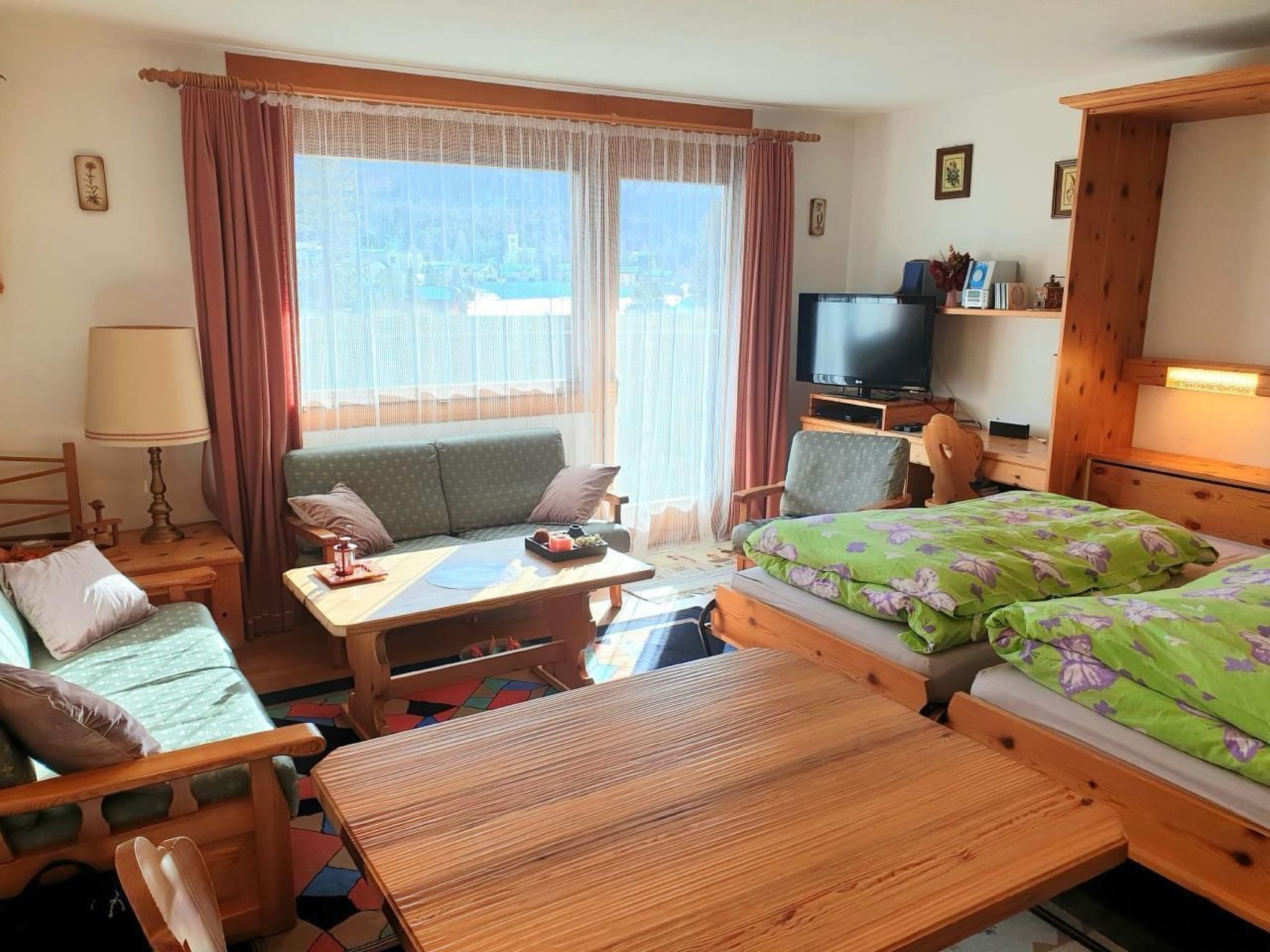 Ein gemütliches Zimmer mit einer Couch, einem kleinen Tisch, einem Bett mit floralem Bettbezug, einem Fernseher und einer Holzkommode.