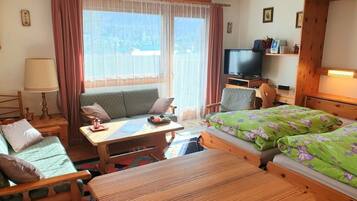 Ein gemütliches Zimmer mit einer Couch, einem kleinen Tisch, einem Bett mit floralem Bettbezug, einem Fernseher und einer Holzkommode.