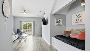 A modern living room with a sofa, a glass coffee table, a ceiling fan, and a TV mounted on the wall. - Lux Ft Walton Beachfront Home MINS to HCA Florida Hospital/ Sleeps 4/ King Bed (Fort Walton Beach)